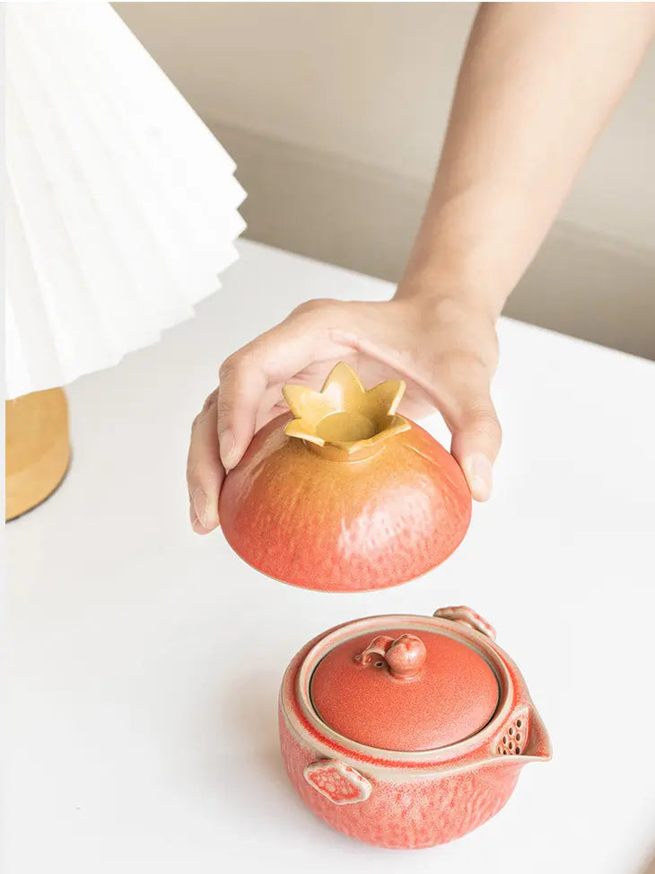 Host cup lifted above the matching coral pomegranate teapot
