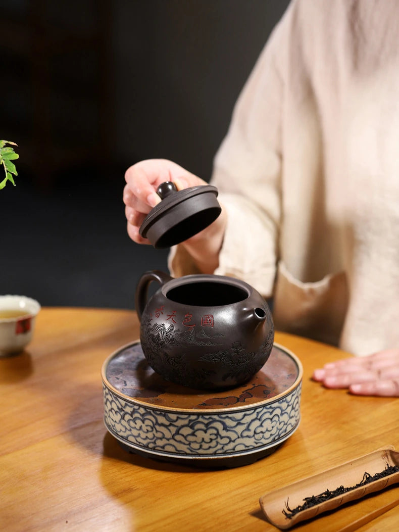 Person removing the lid from the carved Yixing zisha teapot on a decorative tea stand
