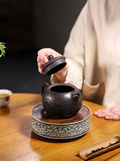 Person removing the lid from the carved Yixing zisha teapot on a decorative tea stand