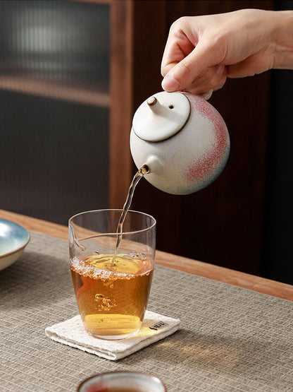 Side-handle ceramic teapot pouring tea into a glass cup