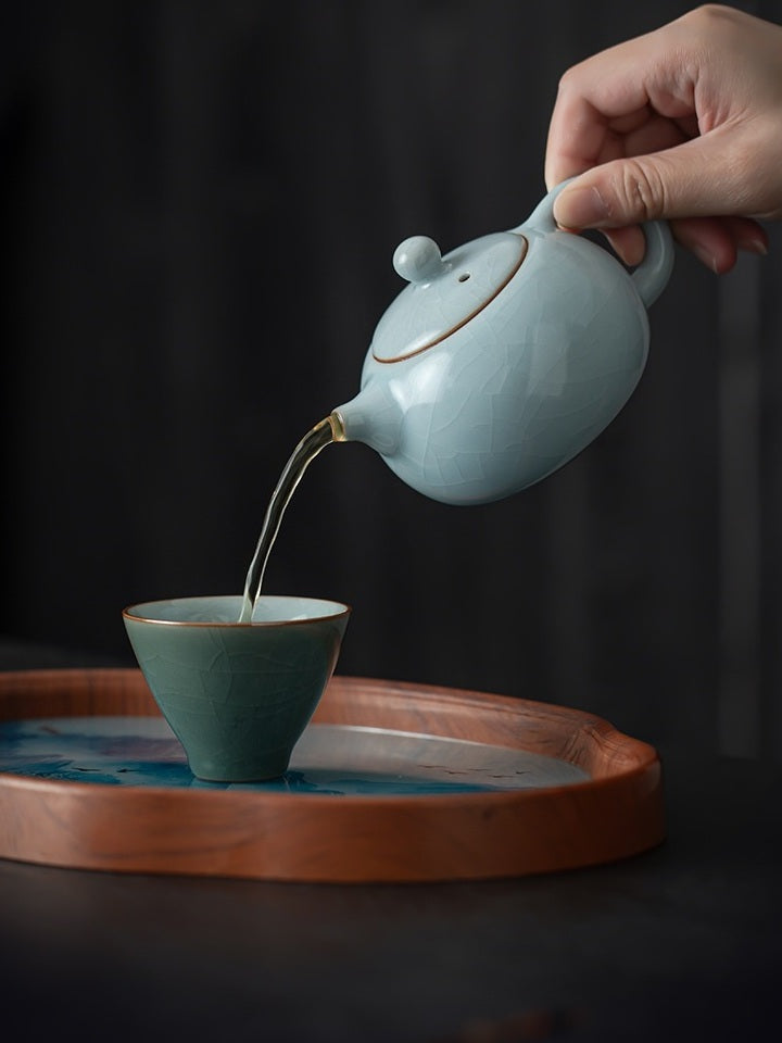 Xishi ceramic teapot pouring tea into a green crackle-glazed tasting cup
