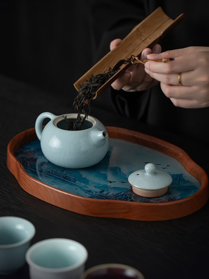 Loose tea leaves being added to an open Xishi teapot on the landscape tea tray
