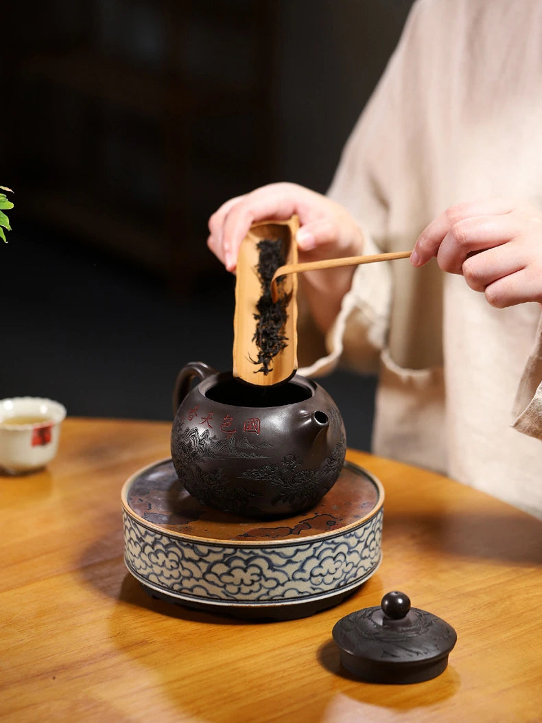 Loose tea leaves being added to the carved Yixing zisha teapot with a wooden tea scoop