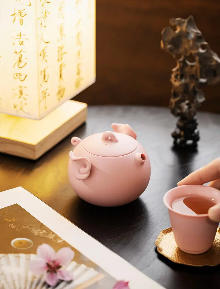Pink zisha pig teapot and matching cup in a warm tea-table setting
