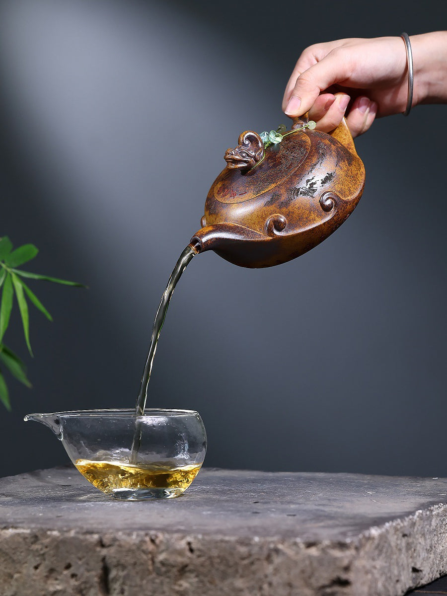 Hand pouring tea from the Yixing zisha wood-fired teapot into a clear glass serving pitcher
