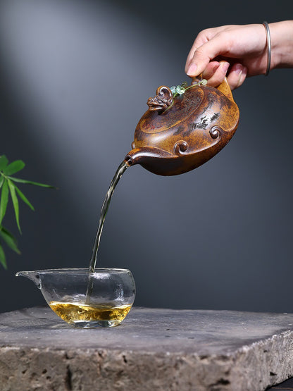 Hand pouring tea from the Yixing zisha wood-fired teapot into a clear glass serving pitcher
