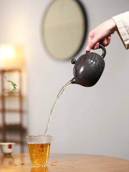Dark brown Yixing zisha teapot pouring amber tea into a clear glass cup