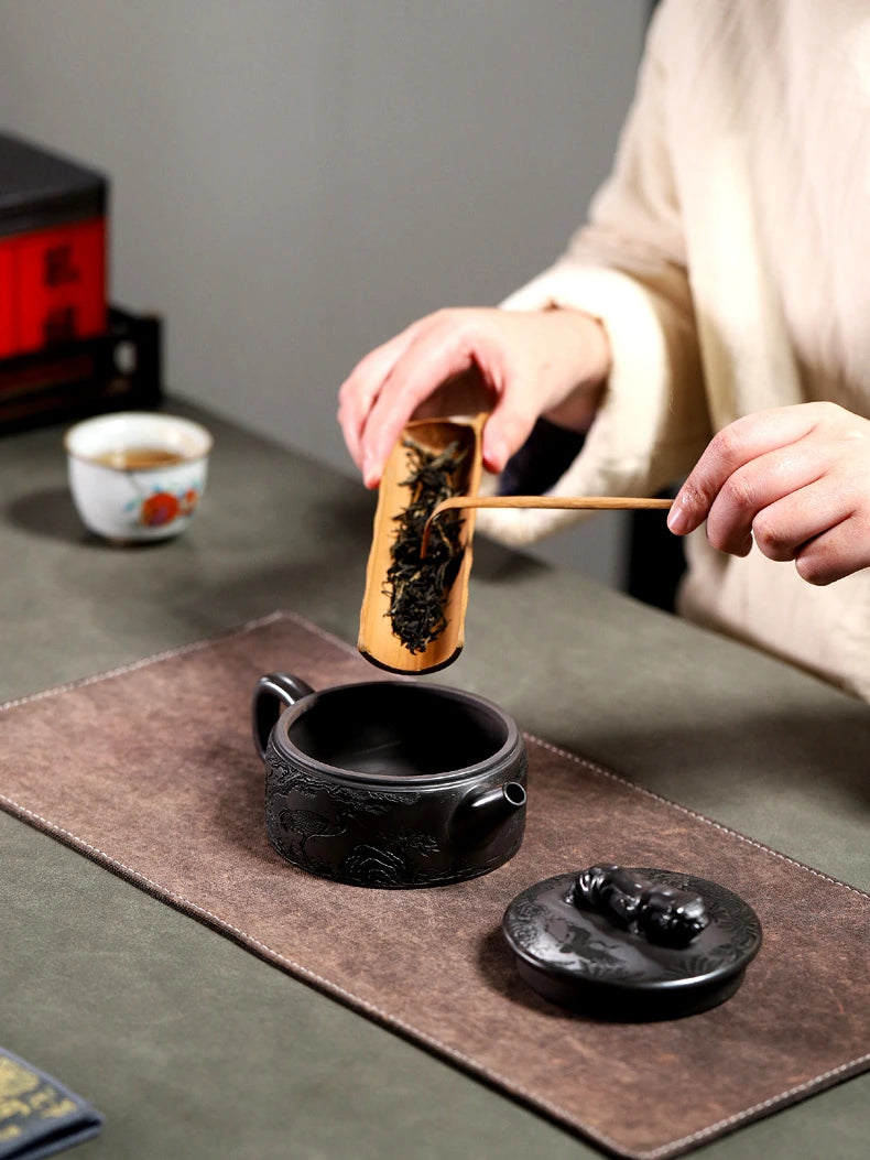 Loose tea leaves being added to the open Yixing zisha teapot with a wooden scoop