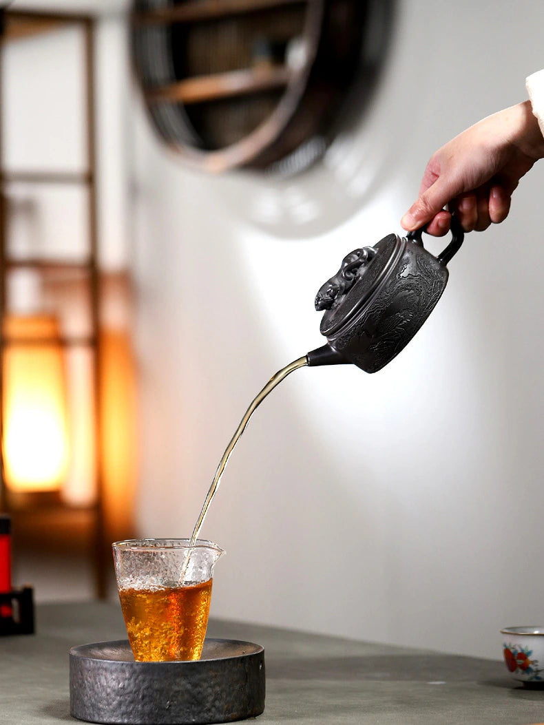 Hand pouring amber tea from the carved Yixing zisha teapot into a clear glass cup
