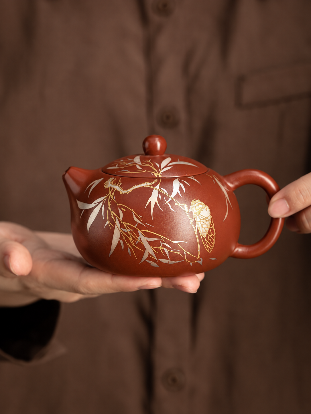 Handheld Xishi zisha teapot showing rounded form and cicada motif
