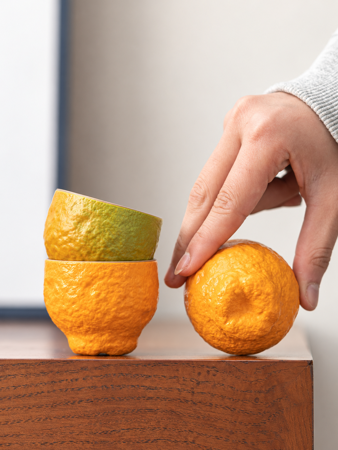 Stacked green-to-orange tangerine-shaped ceramic teacups with a close view of the fruit-like base